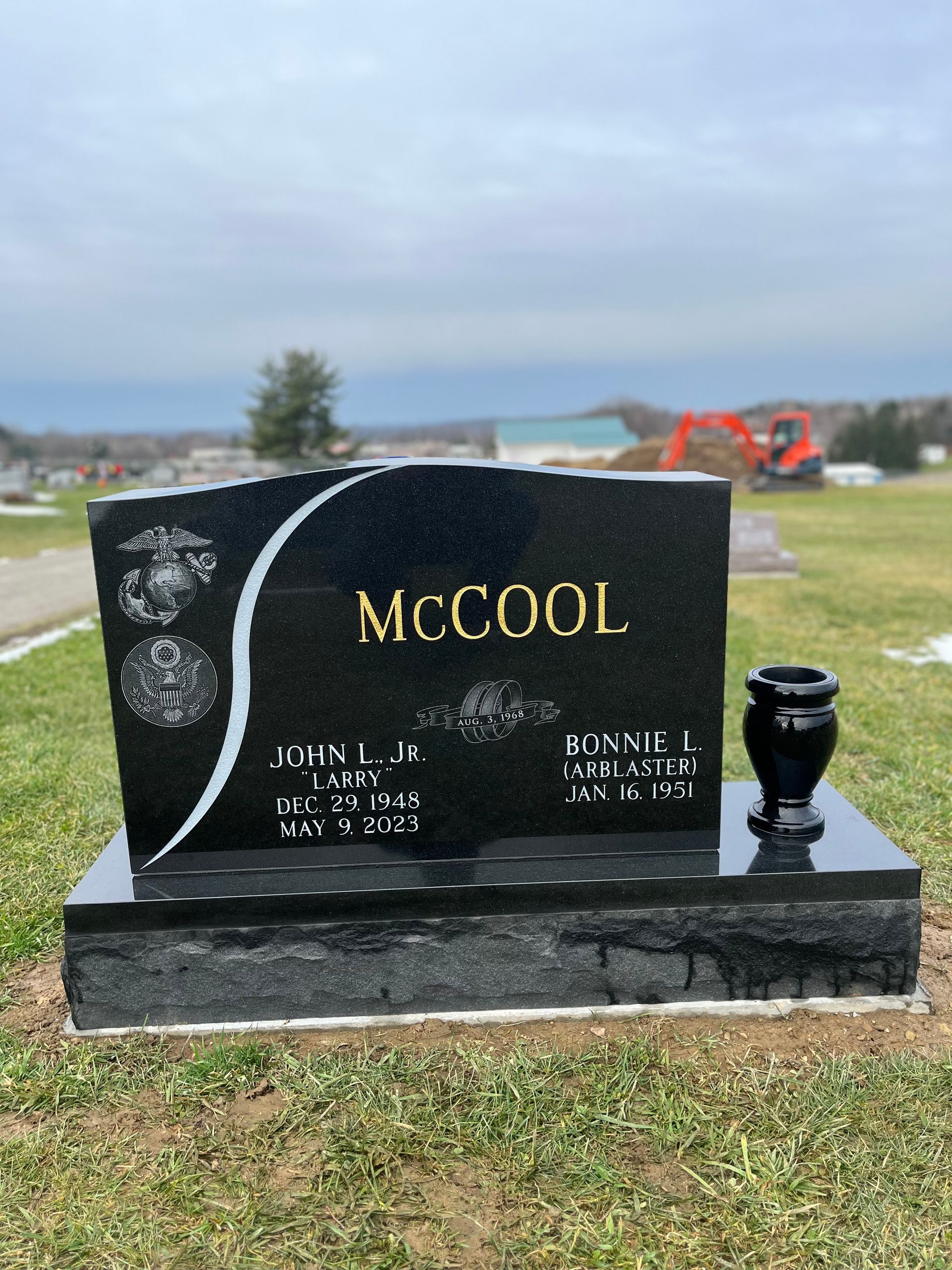 Black gravestone engraved “MCCOOL” in a cemetery with a cloudy sky backdrop.