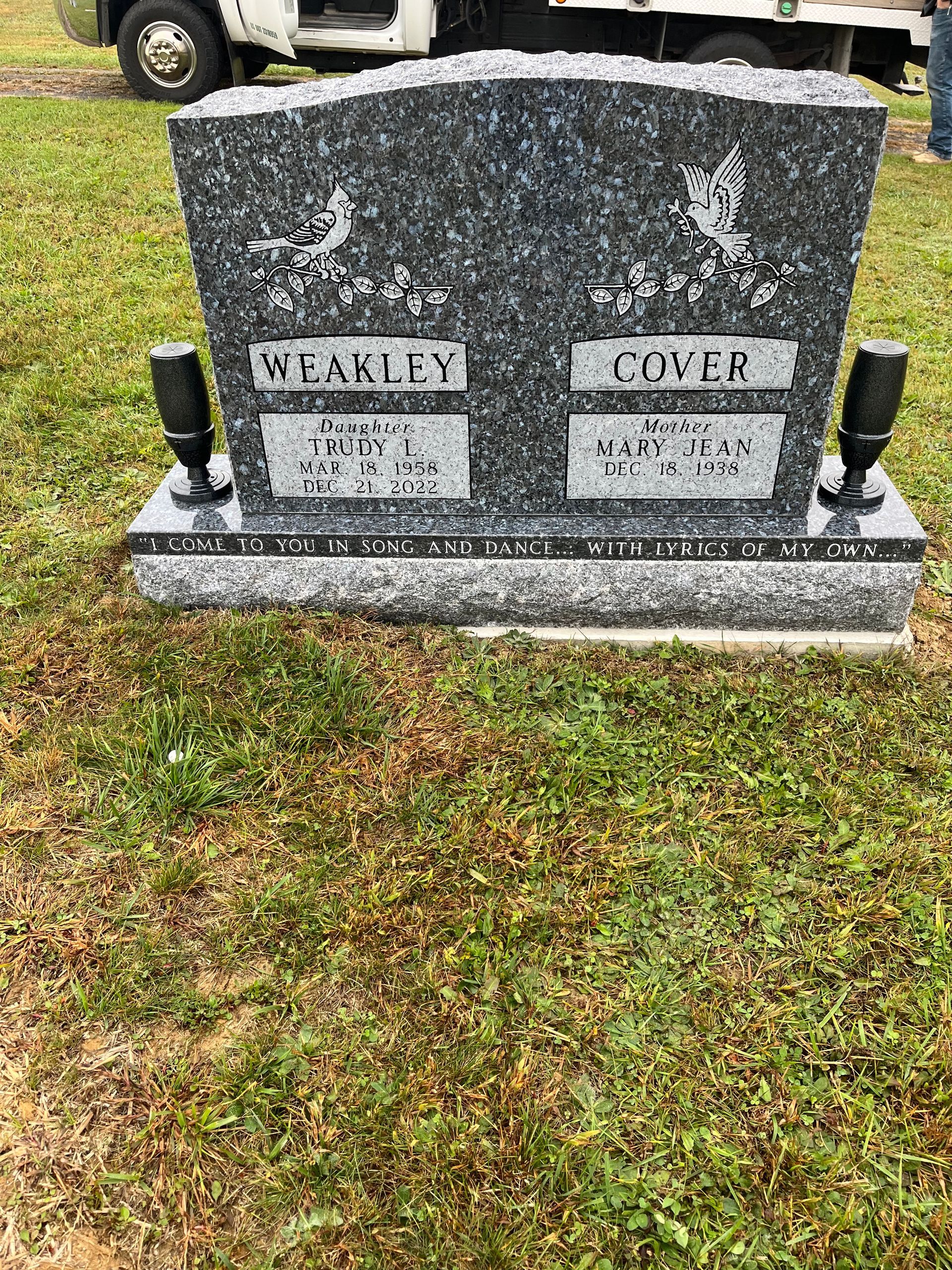 Two gray granite grave markers in a grassy cemetery, with black vases on each side.