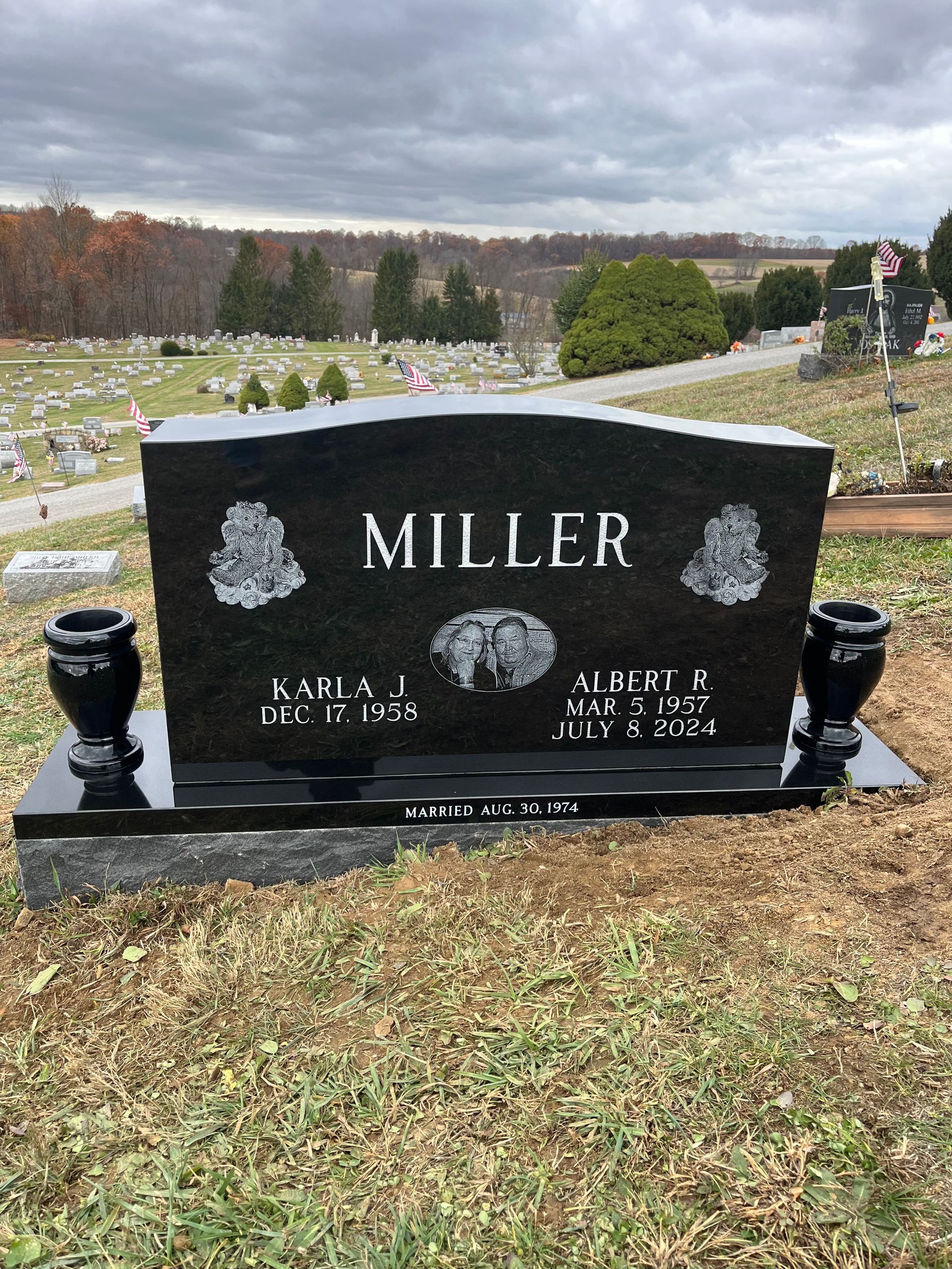 Black Miller gravestone in a cemetery with grassy slopes and many other headstones in the background