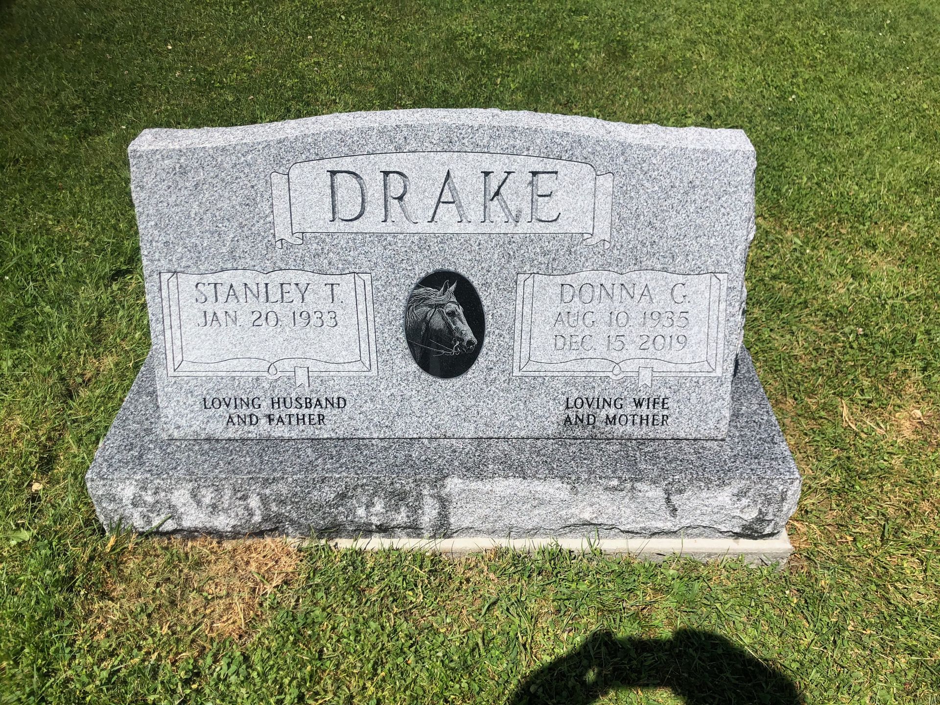 Gray granite Drake family gravestone on grass, with an oval portrait engraving in the center.