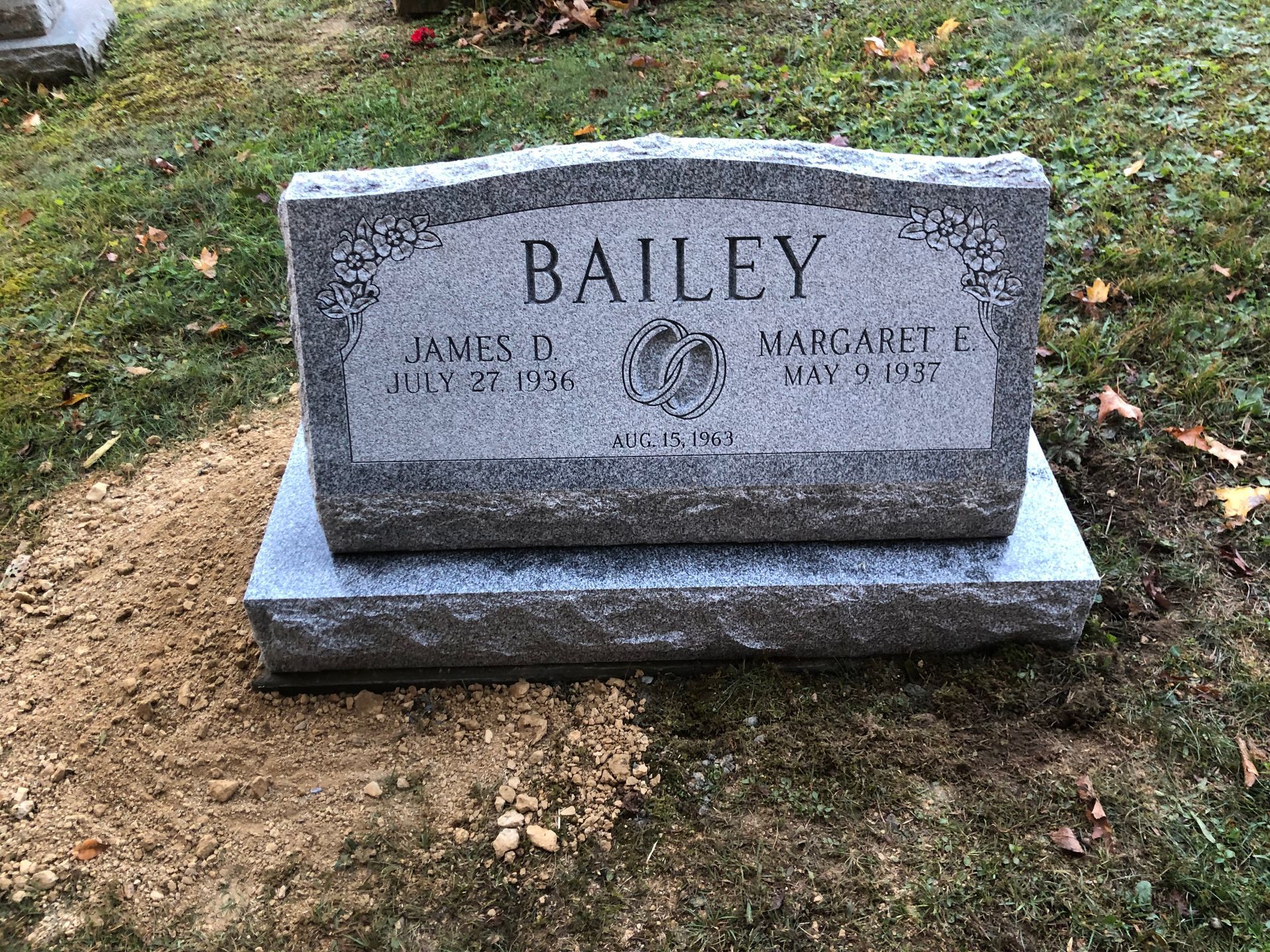 Gray Bailey gravestone on a dirt patch in a grassy cemetery, with engraved names and dates.