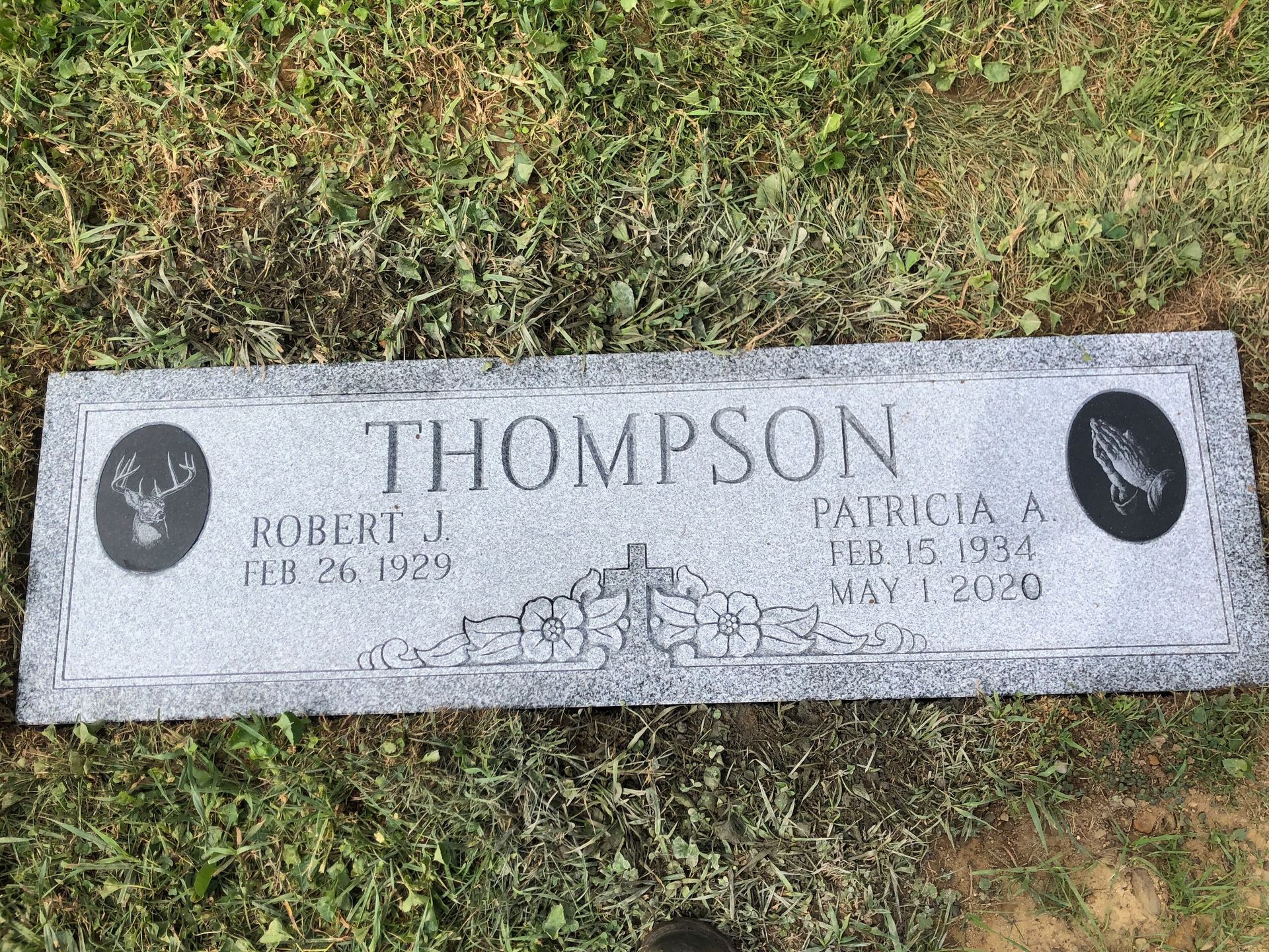 Gravestone engraved “THOMPSON” on a lawn, with two oval portrait plaques and names/dates at the bottom.