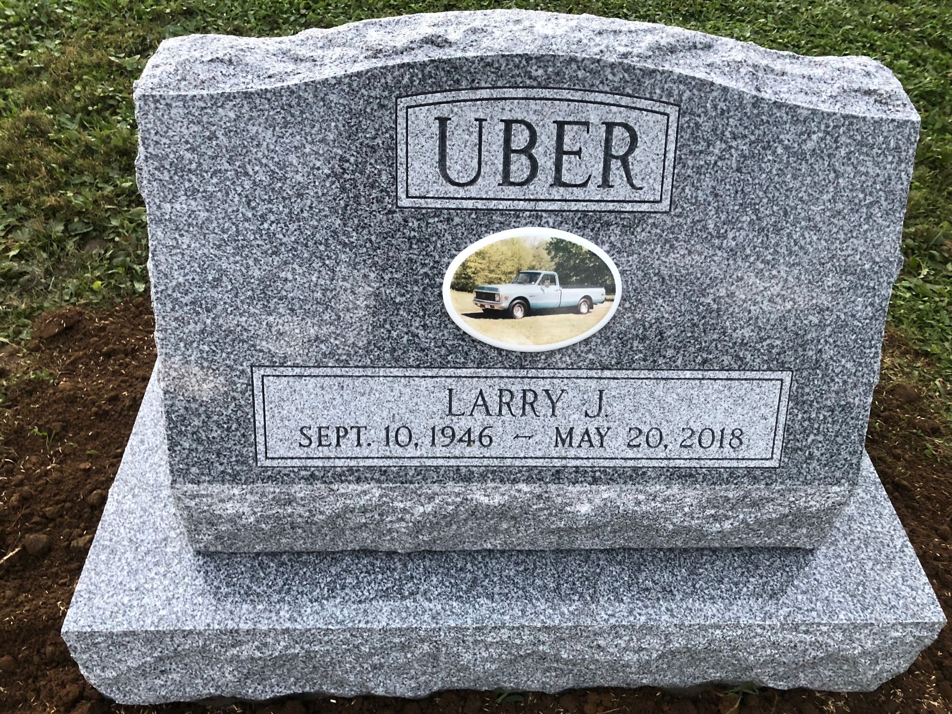 Gray memorial headstone engraved “UBER” with a small oval photo and the name Larry J.