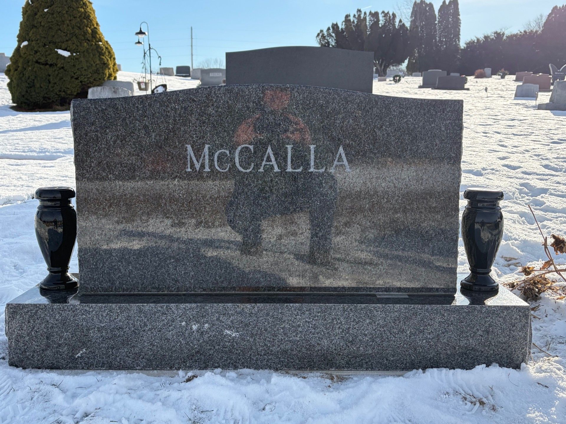 McCalla granite gravestone in a snowy cemetery with two black vases on the base