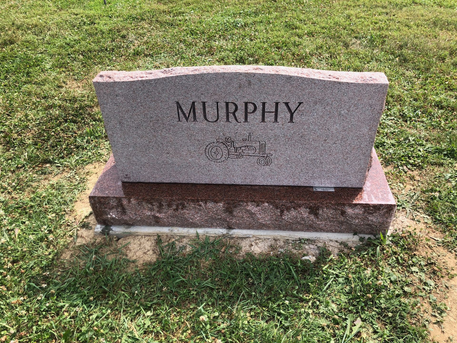 Pink granite gravestone engraved “MURPHY” on a grassy lawn.