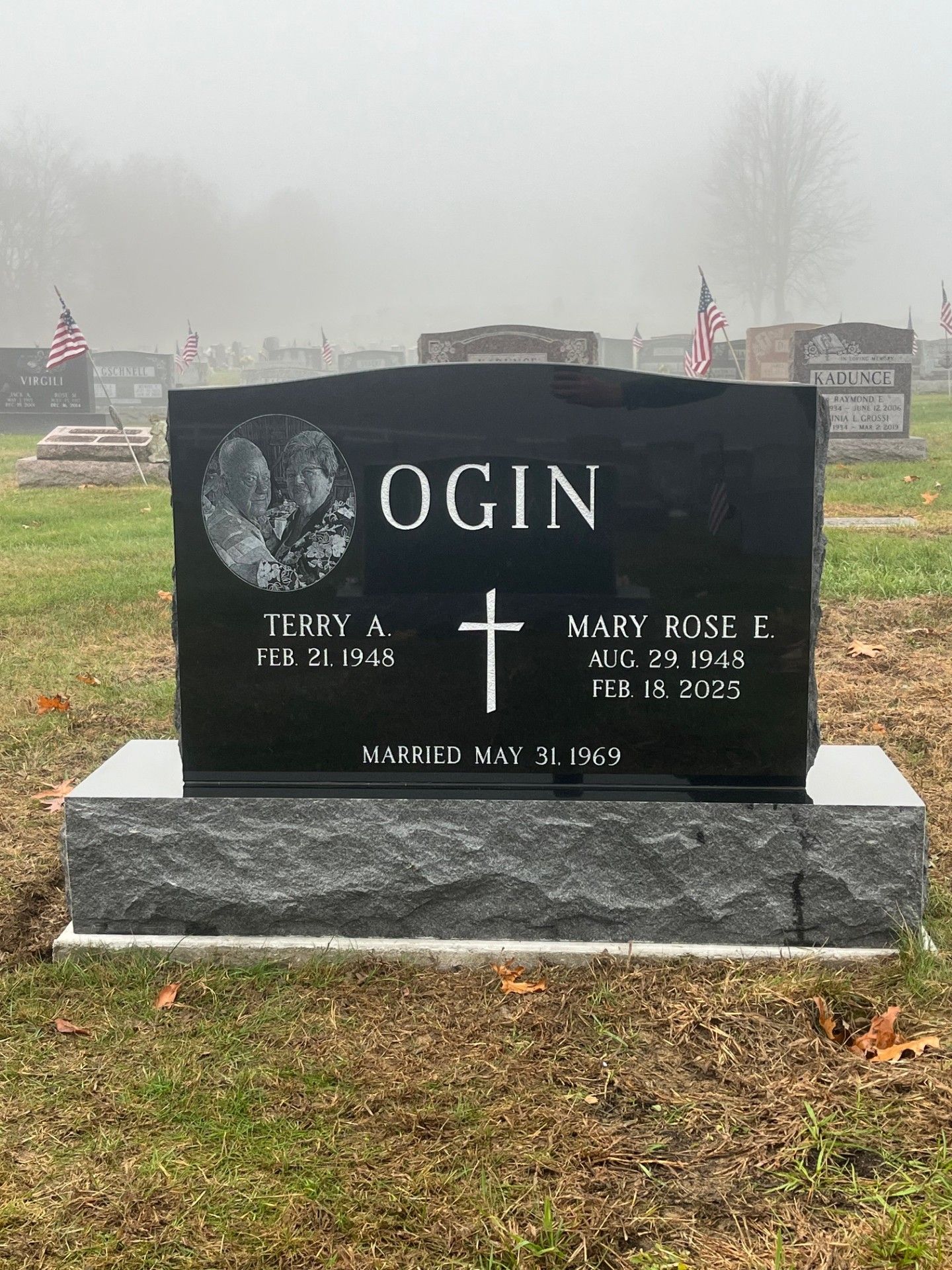 Black granite memorial headstone with white lettering and a cross in a foggy cemetery
