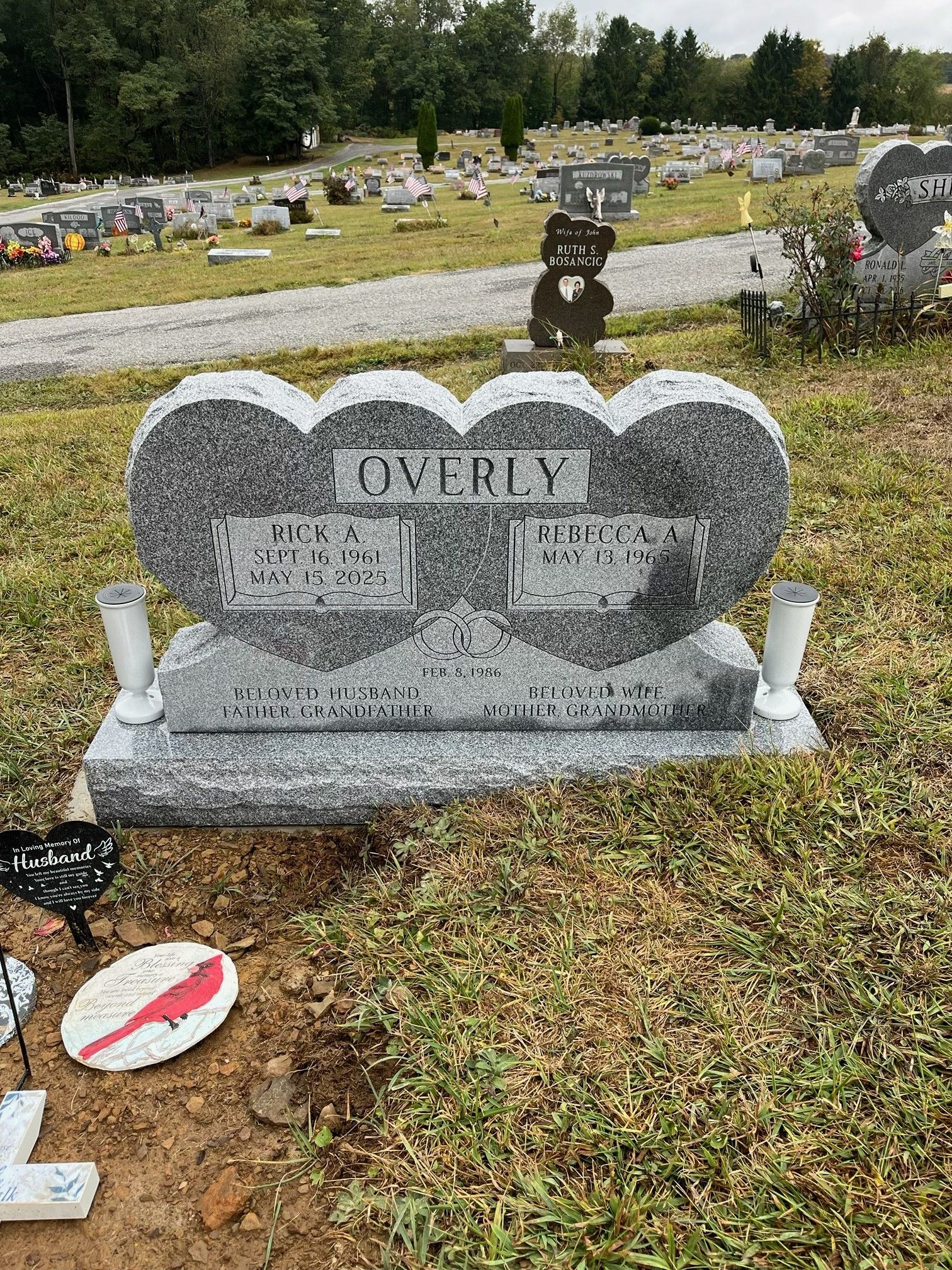 Heart-shaped gray gravestone in a cemetery with white accents and flowers nearby.