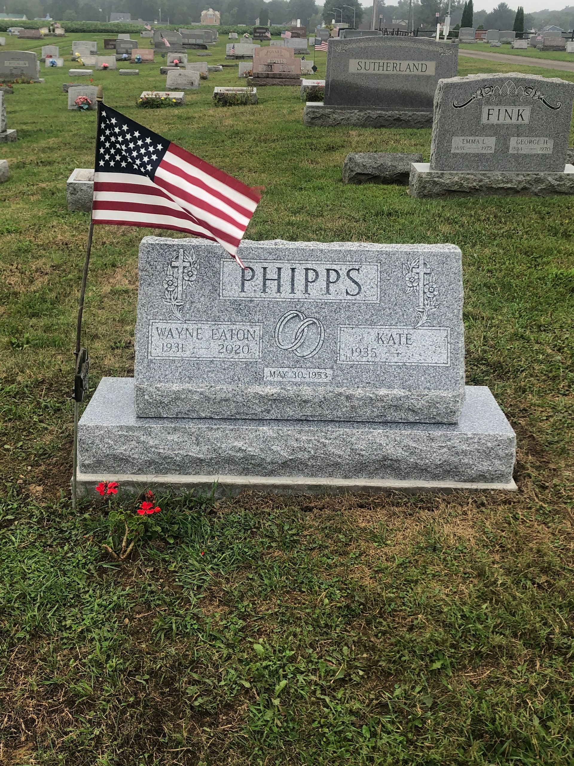 Gravestone in a cemetery with a small American flag planted beside it.