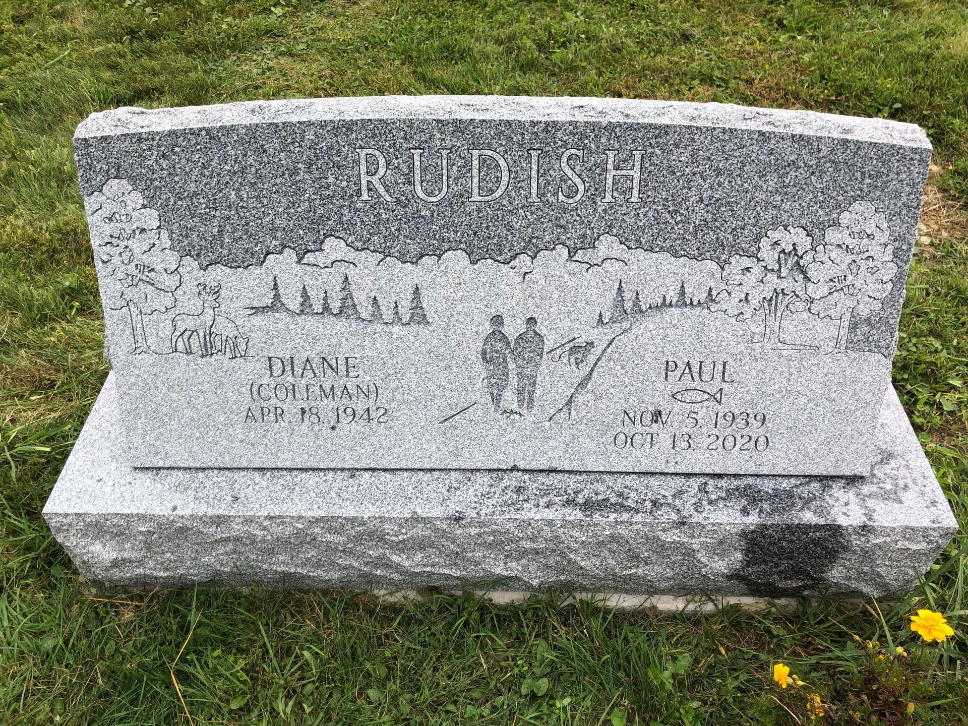Gray granite gravestone with carved cross and floral designs in a grassy cemetery.