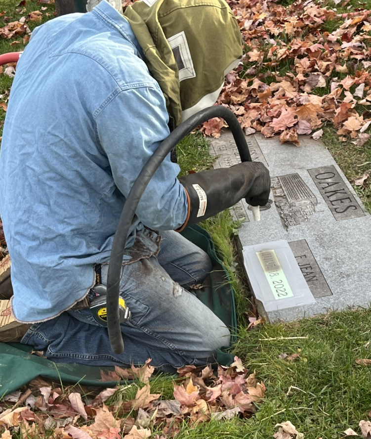 Granite bench in a cemetery, other headstones and flowers visible in the background.