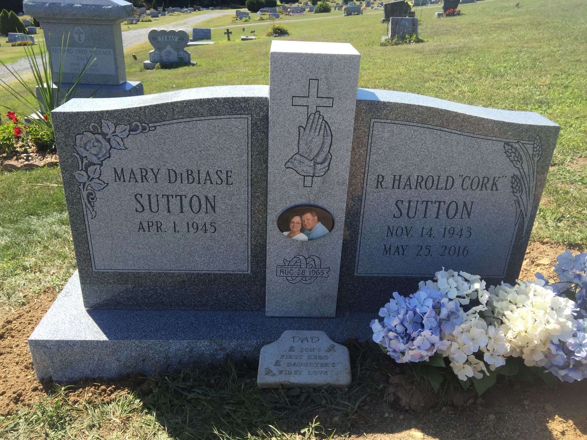 Double gravestone with flowers in a cemetery, one side engraved Mary and the other a second Sutton name.