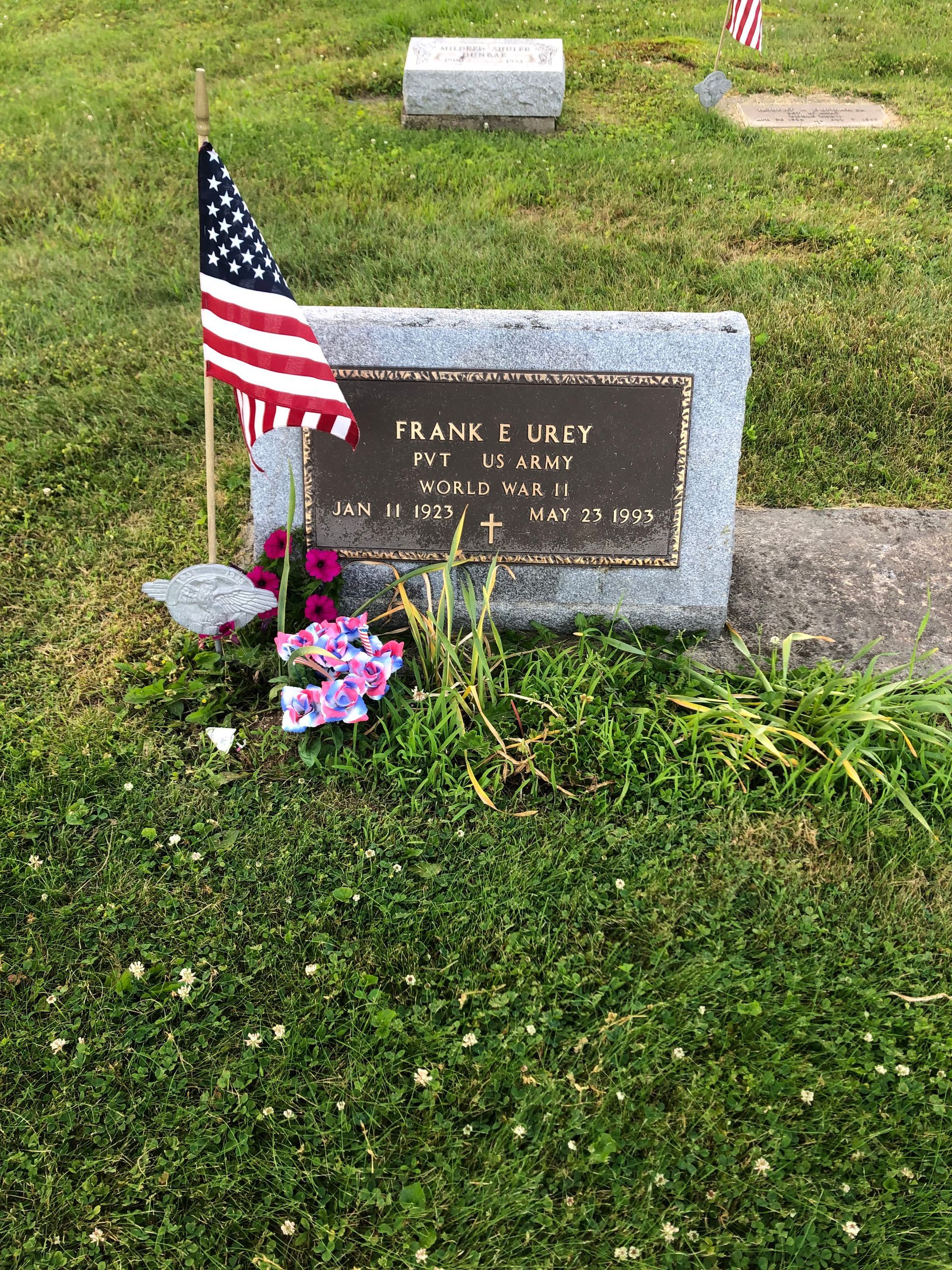 Gravestone in a cemetery with a small American flag and flowers beside it
