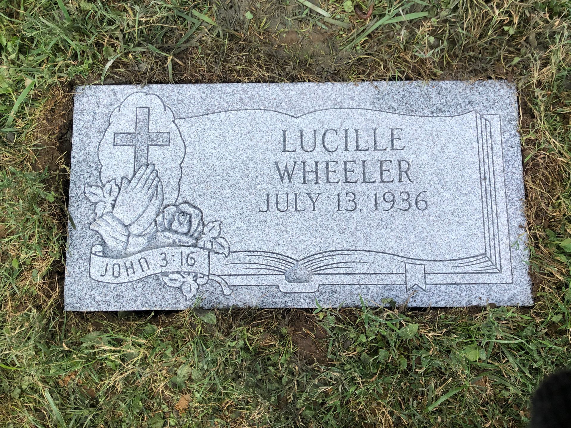 Gravestone in grass for Lucille Wheeler, July 19, 1986, with cross and open book carving