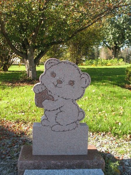 Small stone bear statue holding a heart in a sunny grassy park.