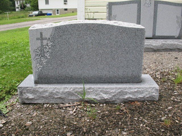 Gray granite gravestone with engraved cross, set on a stone base in a cemetery yard