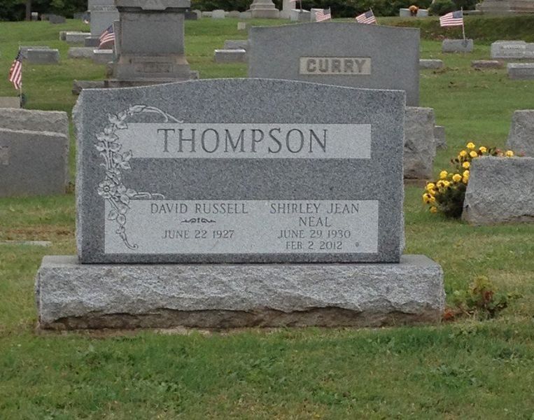 Gray gravestone marked THOMPSON in a cemetery, with yellow flowers nearby.