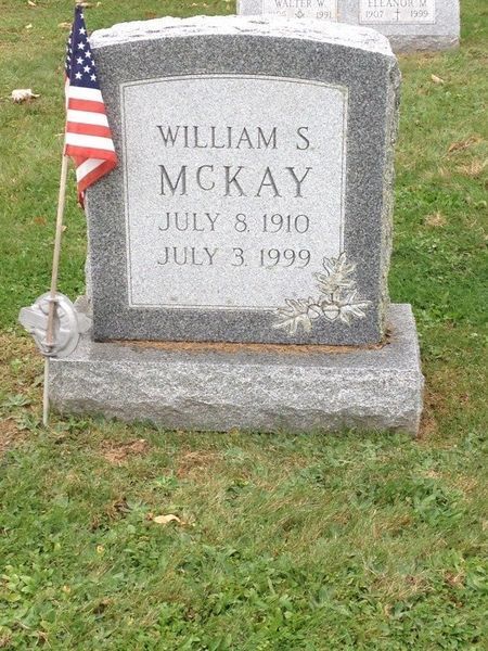 Gravestone for William S. McKay with a small American flag beside it on grass.