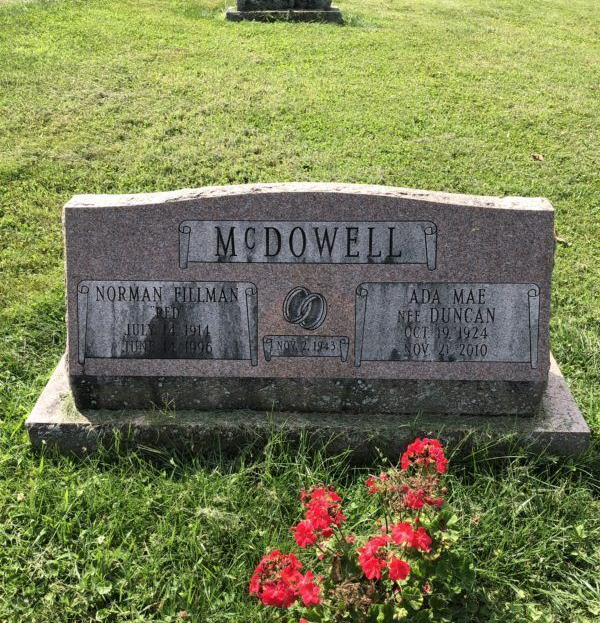 Gravestone engraved “McDowell” in a grassy cemetery with red flowers at the base