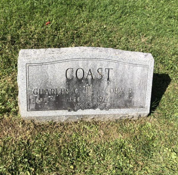 Gray stone grave marker reading “COAST” in a grassy cemetery plot.