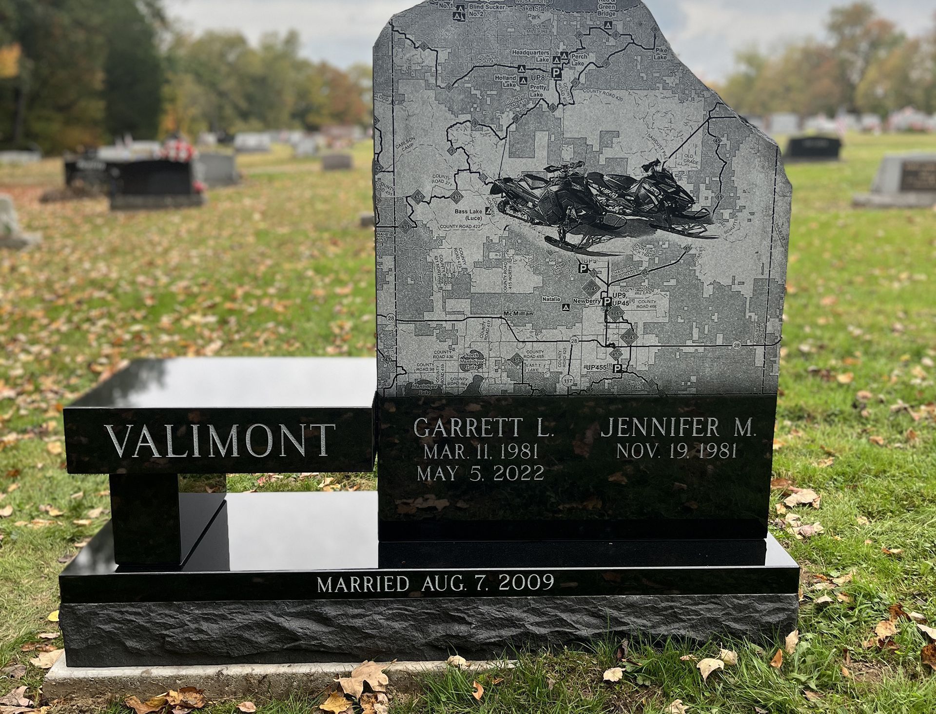 Cemetery with numerous headstones on a grassy lawn; trees casting shadows.