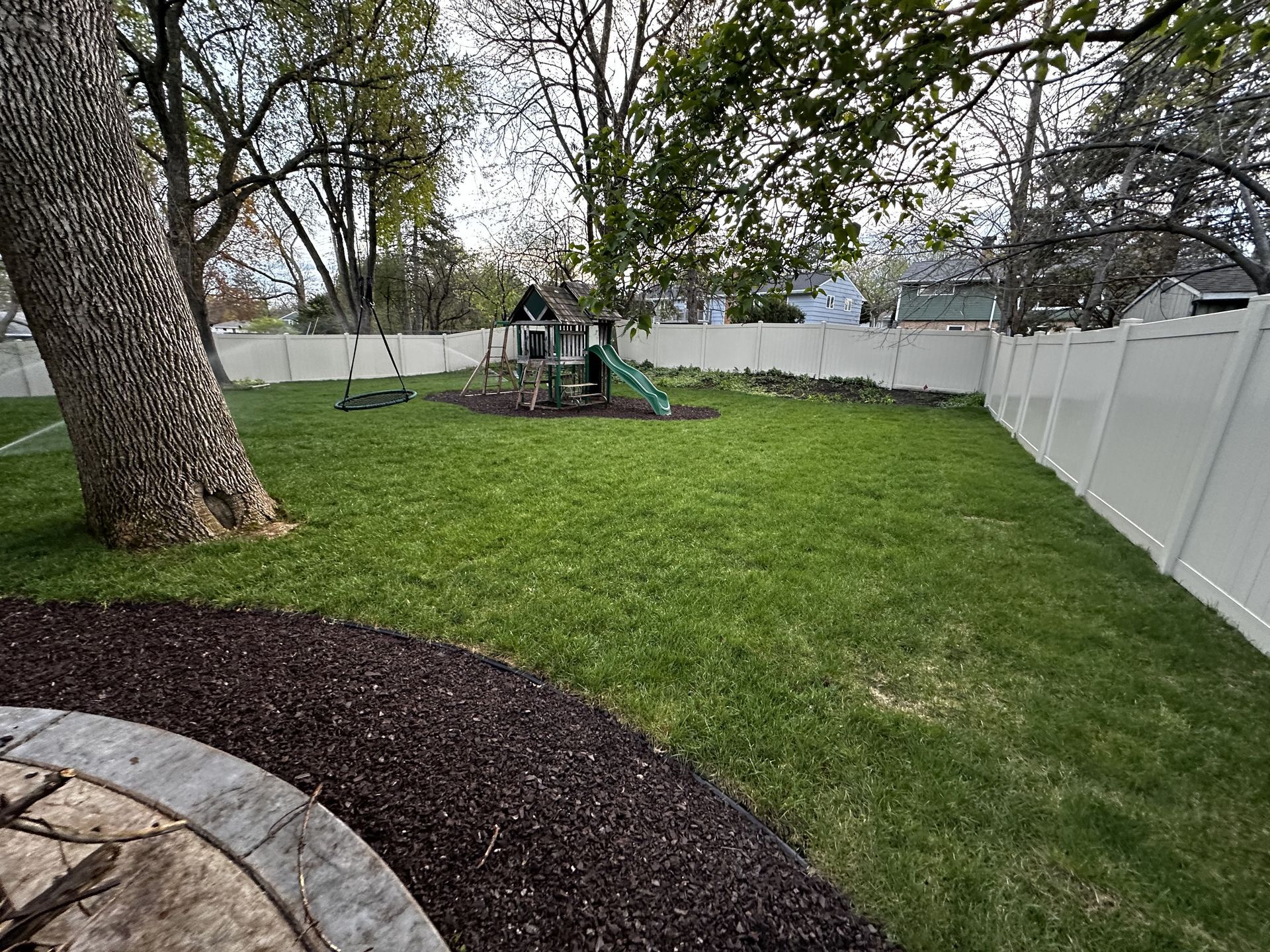 A backyard with a playground and a white fence.
