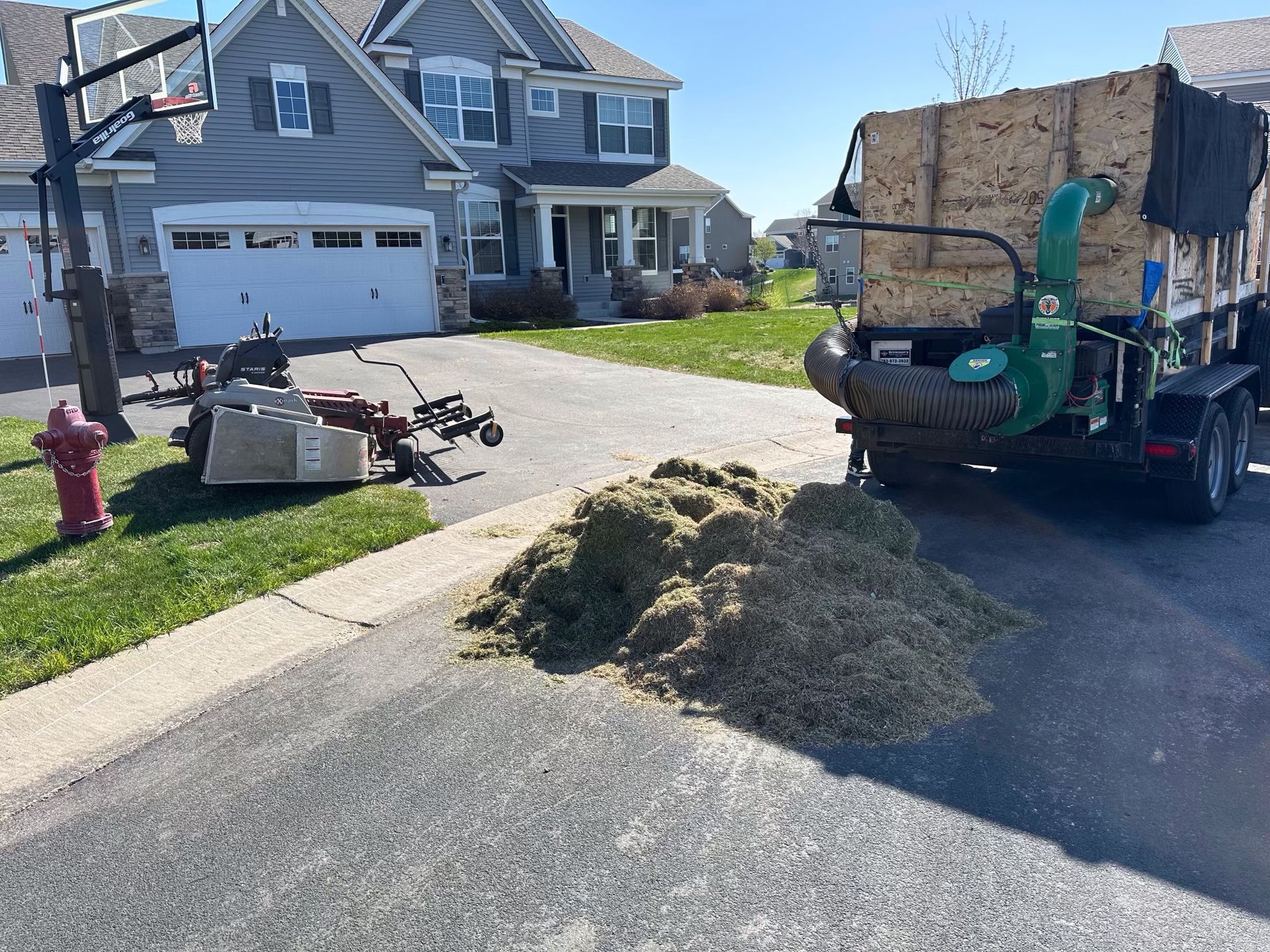 A pile of grass is on the side of the road in front of a house.