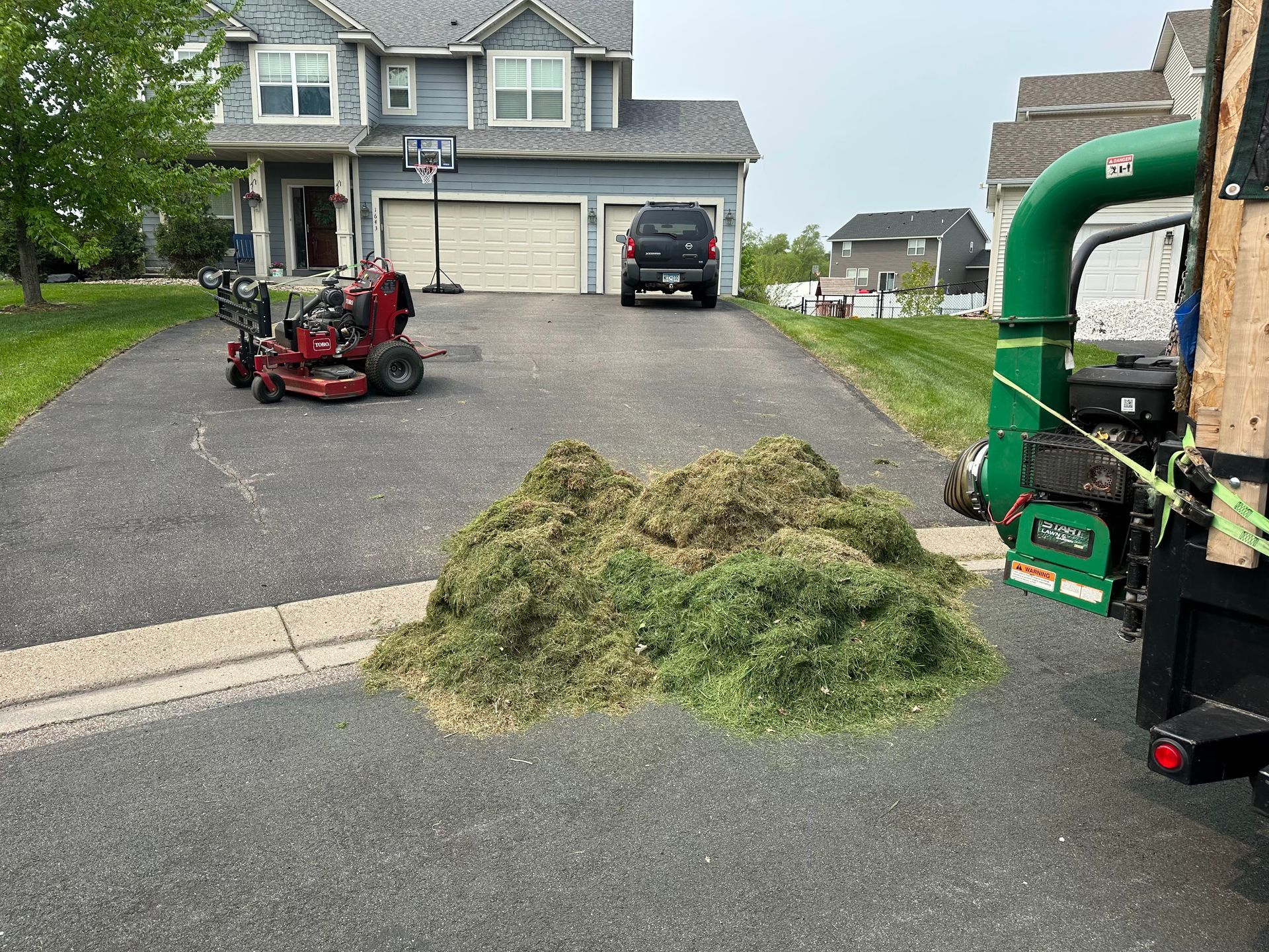 A lawn mower is parked in a driveway next to a pile of grass.