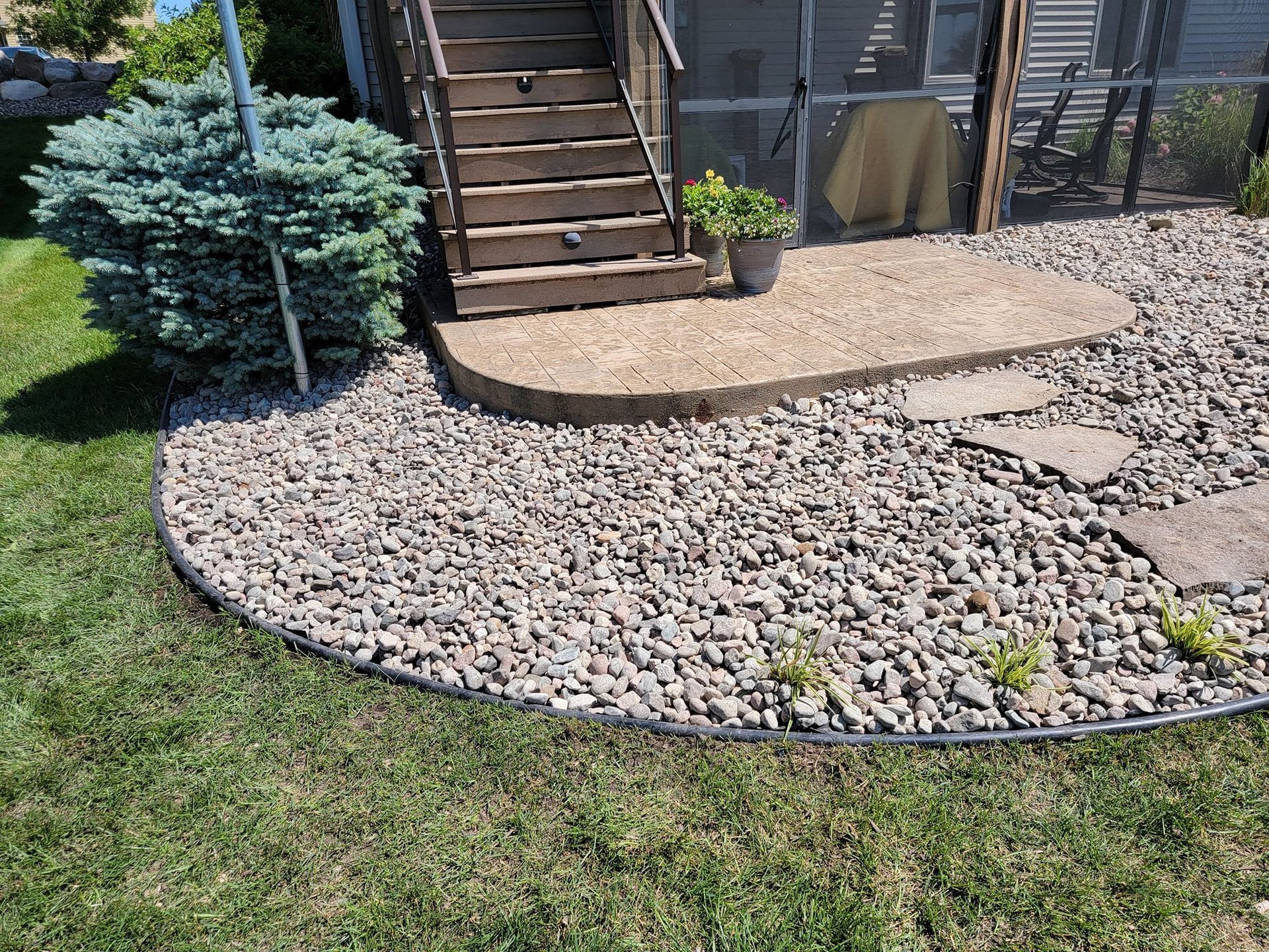 A gravel patio with stairs leading to a screened in porch.