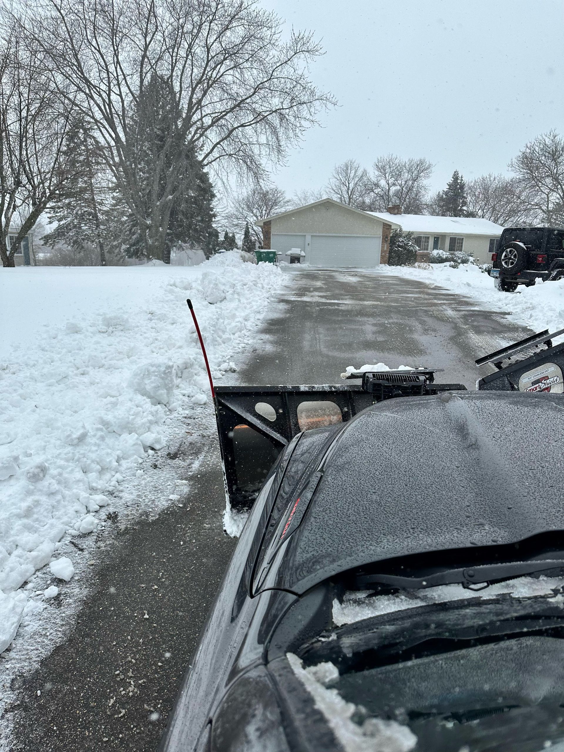 A snow plow is clearing a snowy driveway in front of a house.