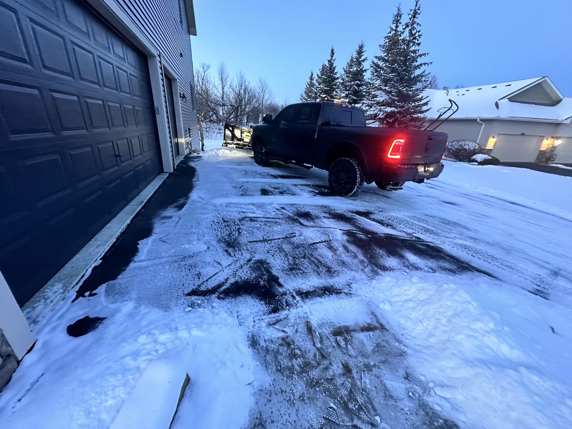 A black truck is parked in the snow in front of a garage door.