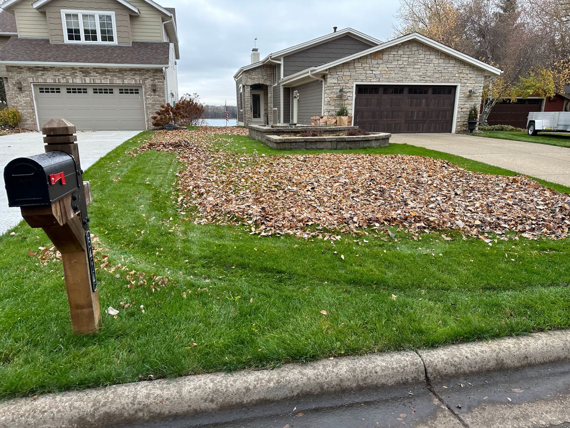 A mailbox is in front of a house with a lot of leaves on the grass.