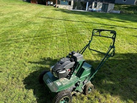 A red lawn aerator is working on a lush green lawn.