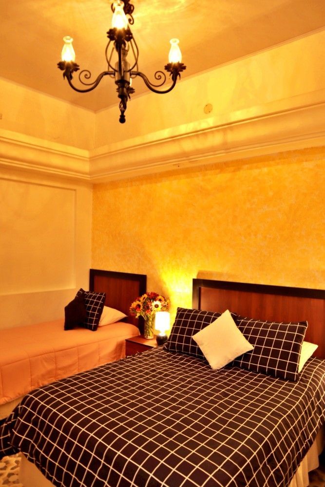 Elegante dormitorio con colcha a cuadros oscuros, iluminación cálida y lámpara de araña en una pared color crema.