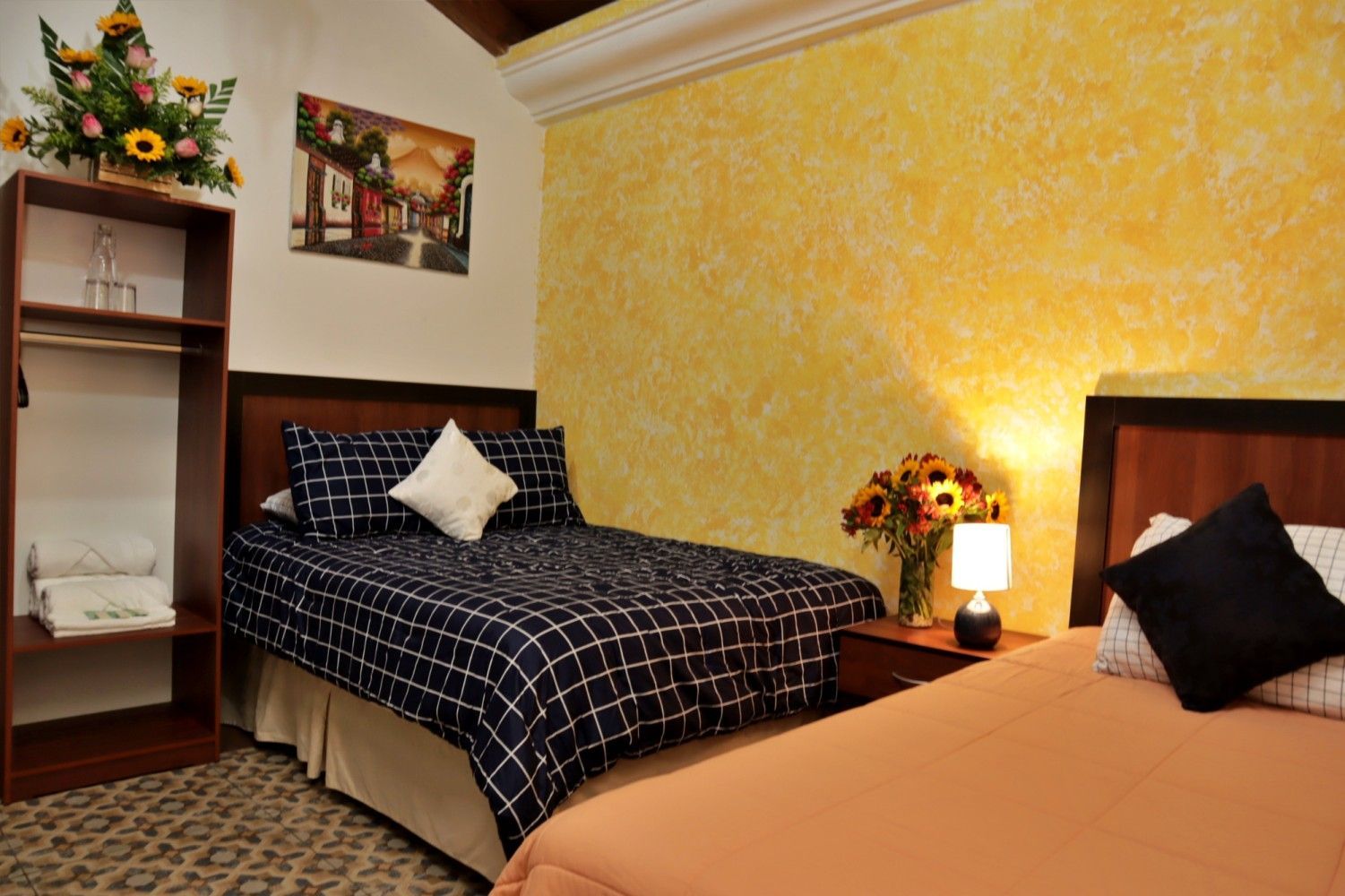 Acogedora habitación con dos camas, paredes de color amarillo cálido, lámpara y decoración floral.