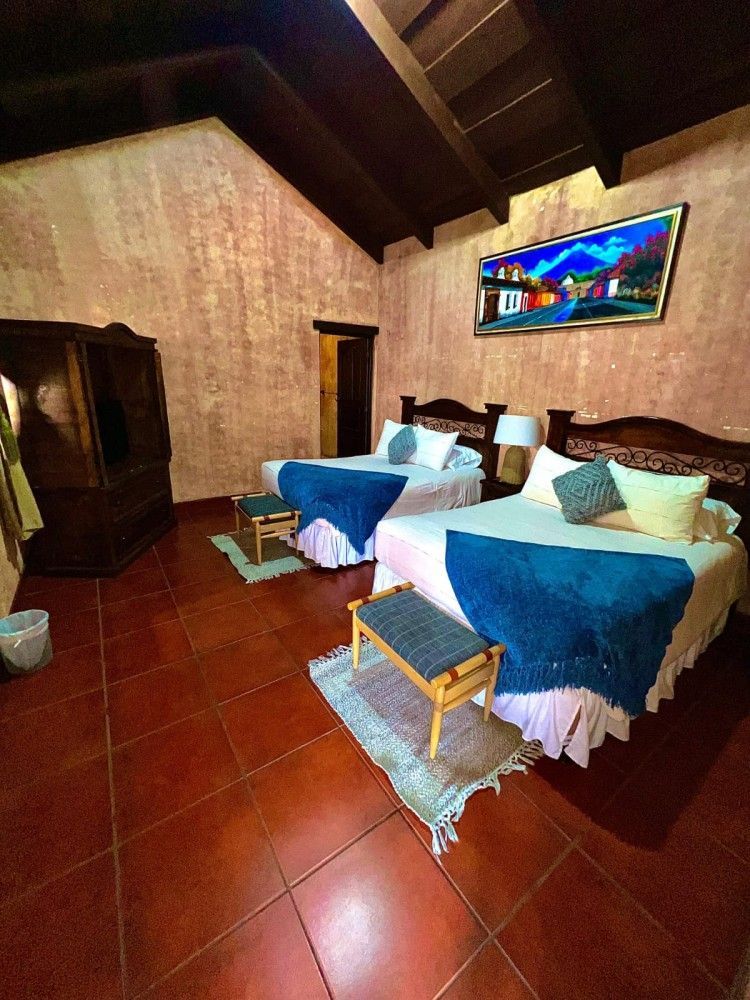 Habitación de hotel rústica con dos camas individuales, suelo de baldosas de terracota y vigas de madera en el techo.