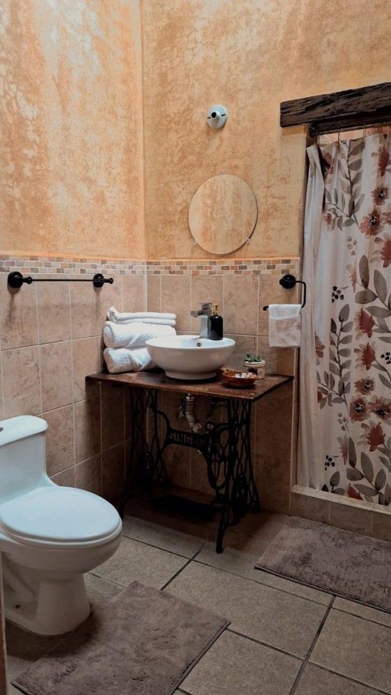 Baño pequeño con inodoro, lavabo con pedestal, cortina de ducha y paredes de color naranja tierra.
