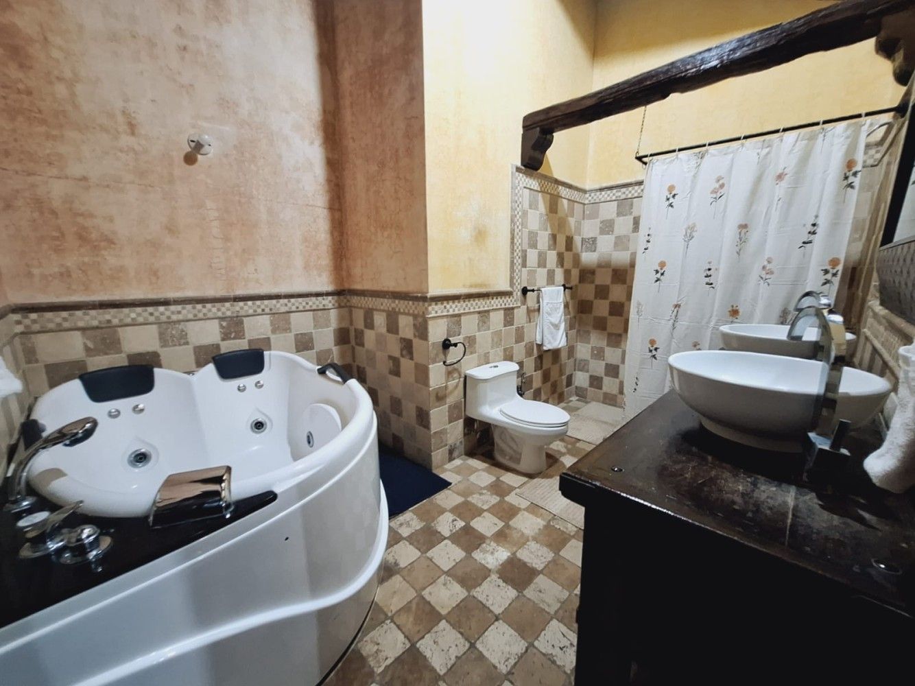 Baño con bañera de hidromasaje en esquina, inodoro, lavabo y cortina de ducha sobre suelo de baldosas.