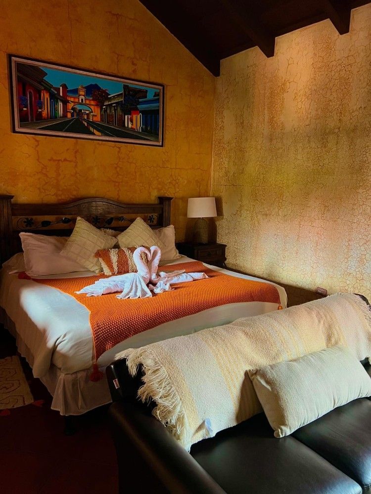 Habitación acogedora con una cama bien hecha, una manta naranja y un pequeño cisne de toalla sobre las almohadas.