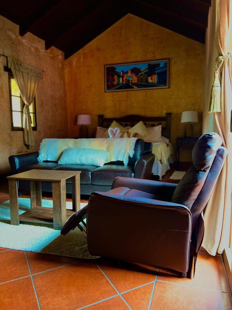 Acogedora habitación rústica con dos camas individuales, sillón de cuero, mesa de madera y suelo de baldosas de terracota.