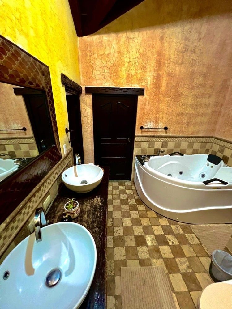 Baño alicatado con dos lavabos, una bañera de hidromasaje en la esquina y paredes amarillas.