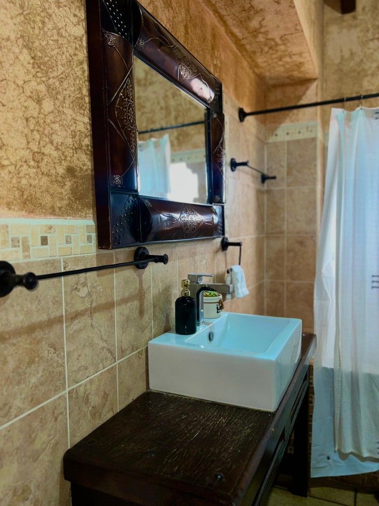 Lavabo pequeño con espejo, barras de apoyo en la pared y cortina de ducha junto a la ventana.