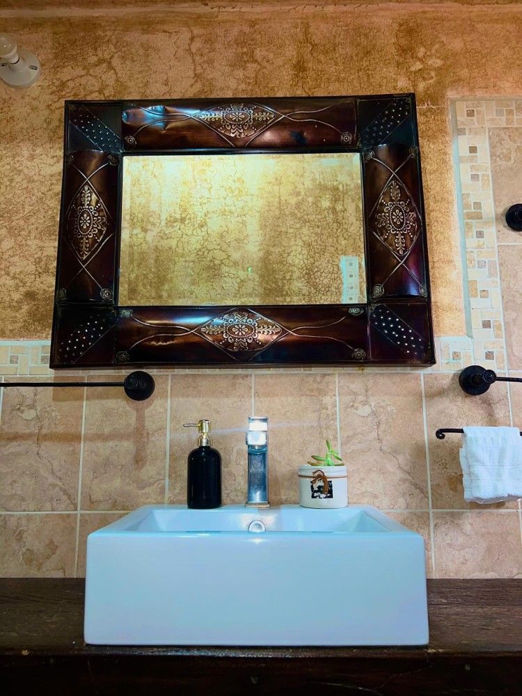 Lavabo de baño moderno con espejo decorativo y pared de azulejos beige.