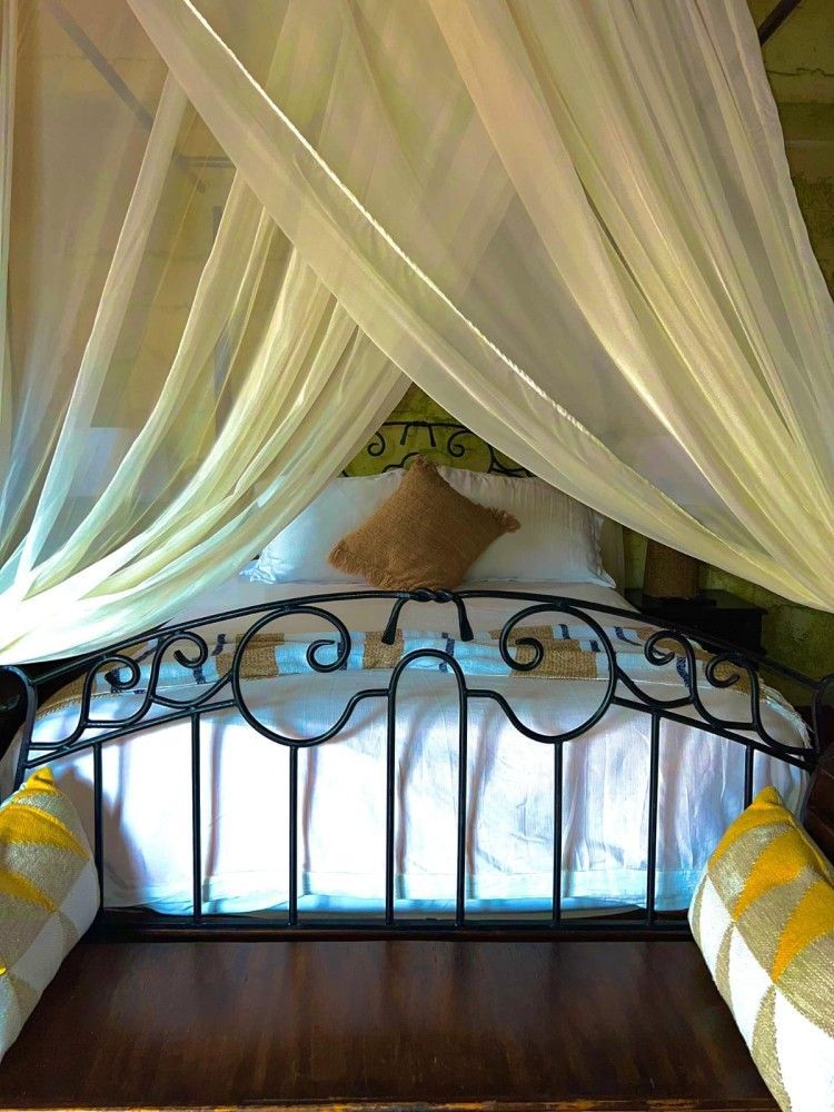 Un dosel transparente cubría una cama de hierro forjado con ropa de cama blanca y azul y almohadas amarillas.