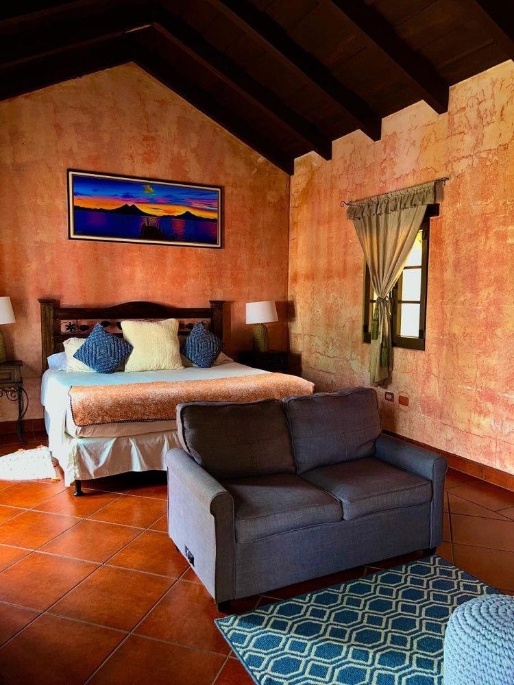 Acogedora habitación con cama, sofá gris, paredes de terracota, suelo de baldosas y ventana con cortinas.