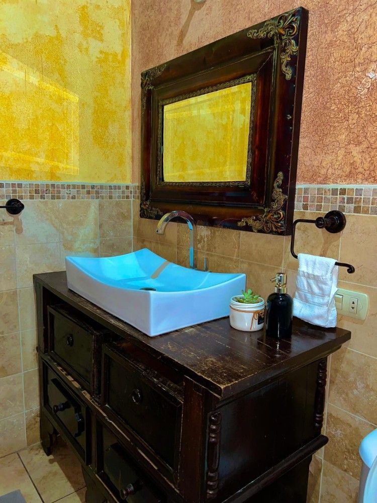 Mueble de baño con armario de madera oscura, lavabo azul, espejo y paredes texturizadas amarillas.
