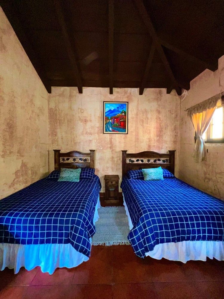 Una pequeña habitación con dos camas individuales cubiertas con mantas de cuadros azules y un cuadro colorido en la pared.