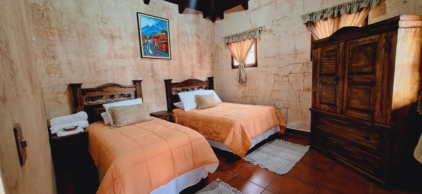 Habitación rústica con dos camas cubiertas de naranja, paredes de piedra y un armario de madera.