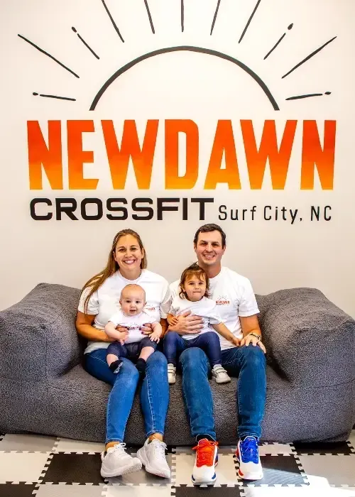 Family seated on a gray couch in front of a New Dawn CrossFit Surf City, NC wall logo