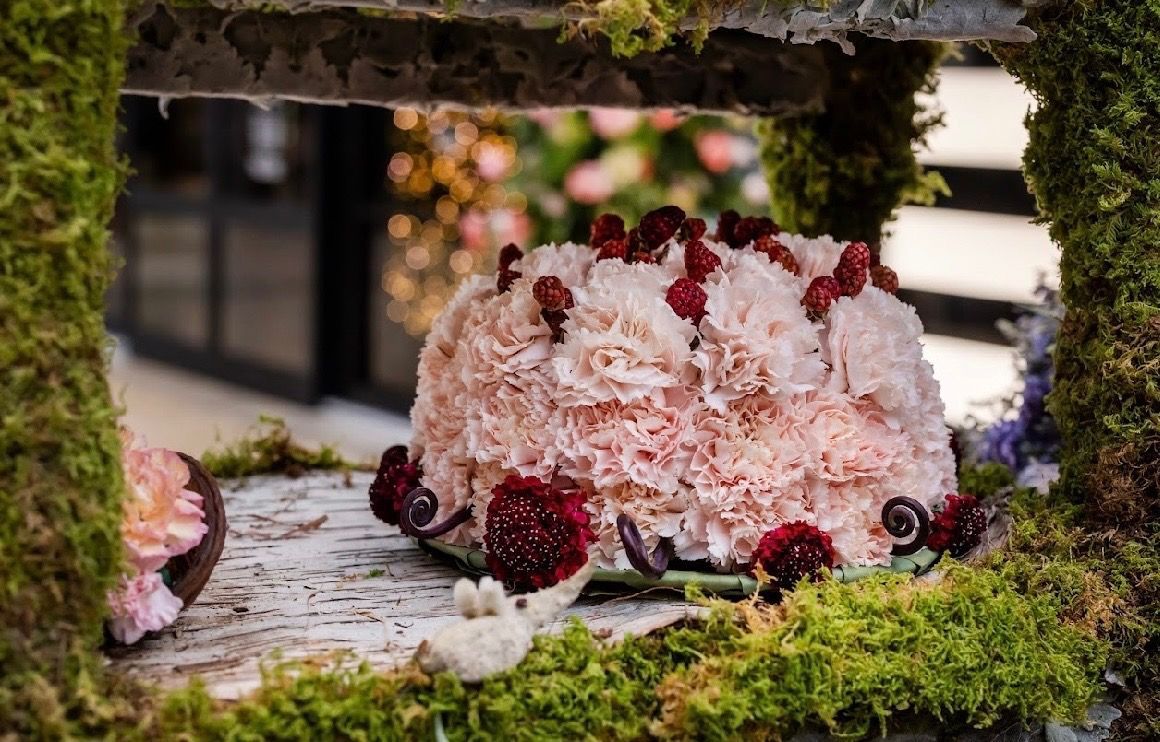 A floral arrangement shaped like a cake, made of light pink carnations and accented with dark red berries and flowers.