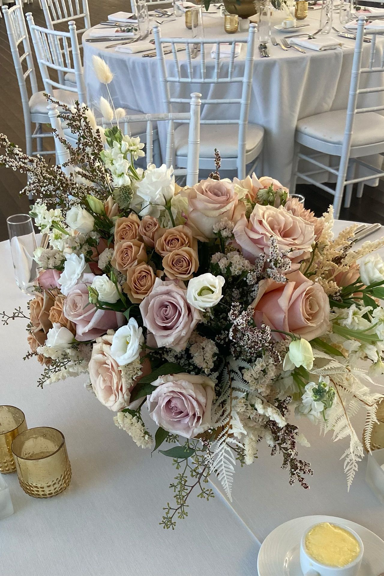 Elegant floral centerpiece of dusty pink roses and white accents on a white table at a formal event.